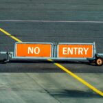 A warning sign indicating no entry on an airport taxiway with a bold yellow line.