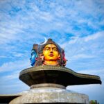Vibrant three-headed Shiva statue under a blue sky in Pokhara, Nepal.