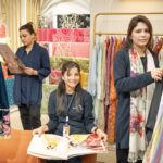 Three women looking at colorful fabrics in a clothing store, showcasing vibrant textile designs.