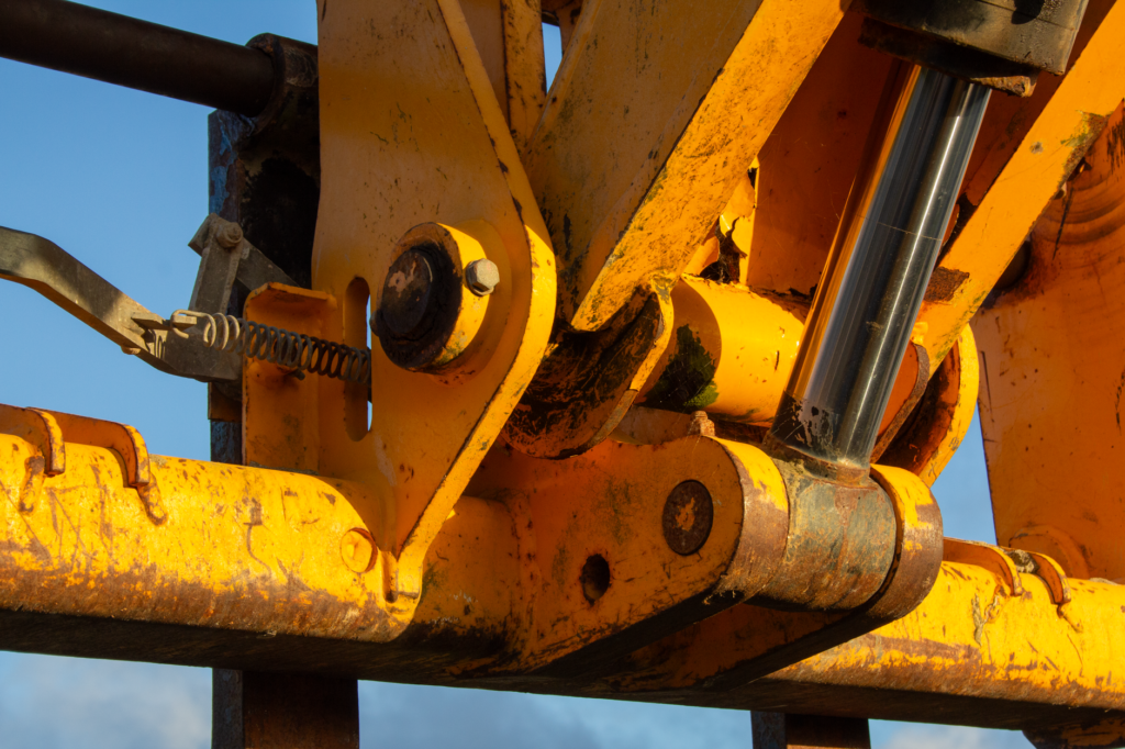 Detailed view of yellow construction equipment's hydraulic system under sunlight.