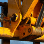 Detailed view of yellow construction equipment's hydraulic system under sunlight.