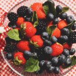 A vibrant mix of strawberries, blackberries, and blueberries with mint leaves in a glass bowl.
