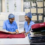 Two female textile workers inspecting fabrics with cheerful expressions in a factory setting.