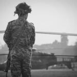 Indian Army soldier in camouflage watches over military helicopter at Kolkata airfield.