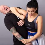 Woman in sports bra demonstrating self-defense martial arts against a man indoors.