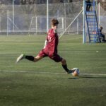 Teenager in action kicking a soccer ball during an outdoor match on a sunny day.