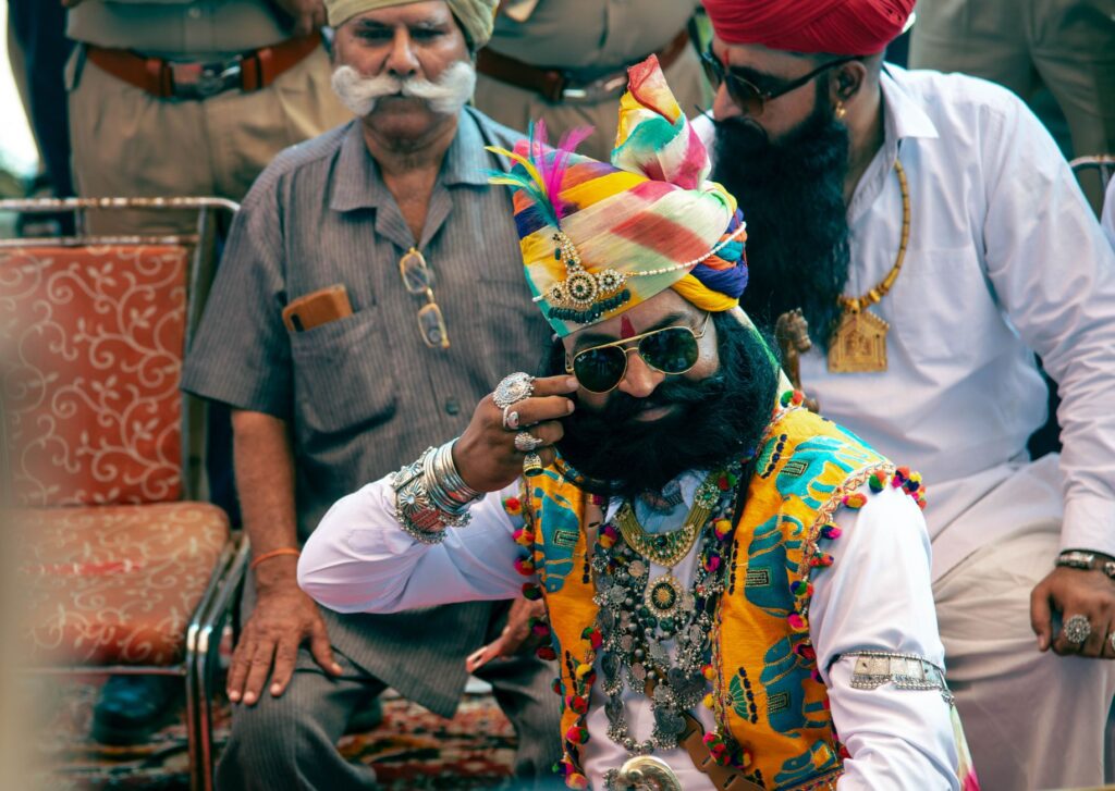 Men in colorful traditional Rajasthani attire with turbans and jewelry at a cultural event.