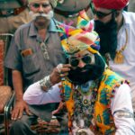 Men in colorful traditional Rajasthani attire with turbans and jewelry at a cultural event.