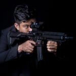 Portrait of a man aiming a rifle with a focused expression against a black background.