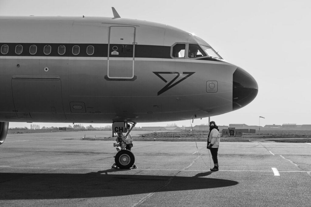 Side view of a commercial airplane on runway with ground staff in monochrome setting
