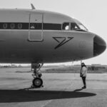 Side view of a commercial airplane on runway with ground staff in monochrome setting