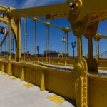 Vibrant yellow suspension bridge standing out against a clear blue sky, showcasing modern engineering.