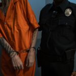 Tattooed prisoner handcuffed in orange jumpsuit beside uniformed officer, highlighting law enforcement.