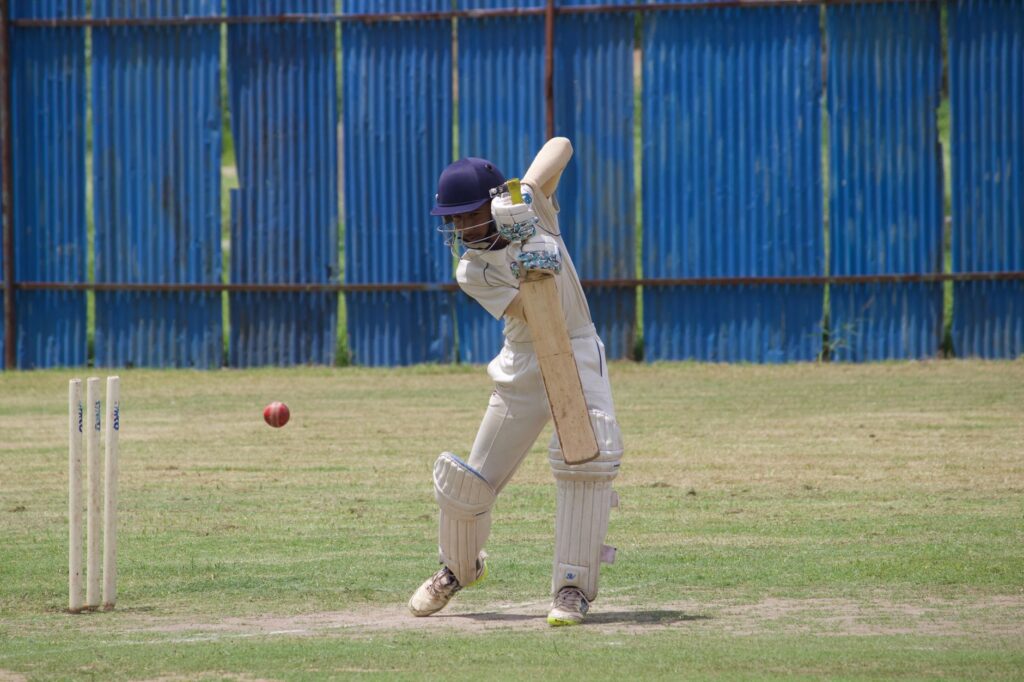 Cricket player in action, batting on a grass field in Gahunje, India.