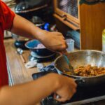 Person cooking shredded meat in a wok on a stove, home kitchen cooking scene.