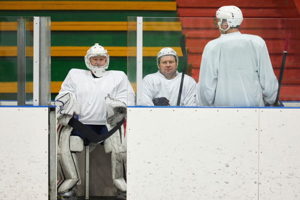 Hockey players in uniforms sitting on the bench during a game pause inside the ice rink.