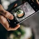 Person photographing delicious Asian dish with a smartphone in a creative setting.