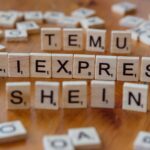 Wooden Scrabble tiles display popular e-commerce platforms on a wooden surface.