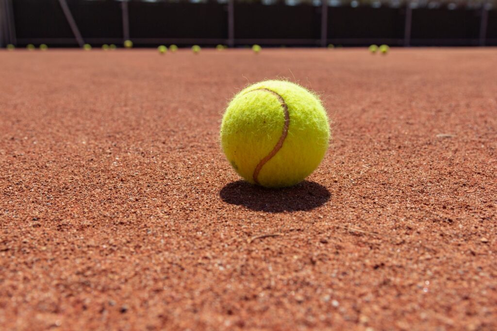Yellow tennis ball on clay court surface, highlighting texture and sports theme.