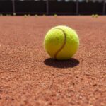 Yellow tennis ball on clay court surface, highlighting texture and sports theme.