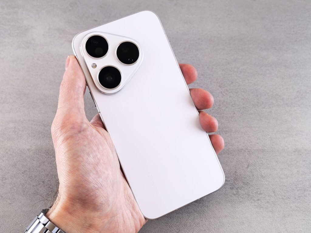 A white smartphone with a triple camera lens held in hand, showcasing its sleek design.