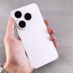 A white smartphone with a triple camera lens held in hand, showcasing its sleek design.