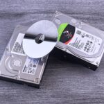 Two computer hard drives and a shiny disk displayed on a wooden surface.