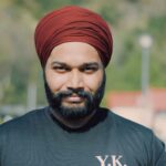 A cheerful man wearing a red turban and black t-shirt enjoys a sunny day outdoors.