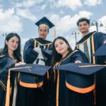 A group of young adults celebrating their graduation with caps and gowns outdoors.