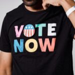 A close-up shot of a black t-shirt with colorful Vote Now text, promoting voting awareness.
