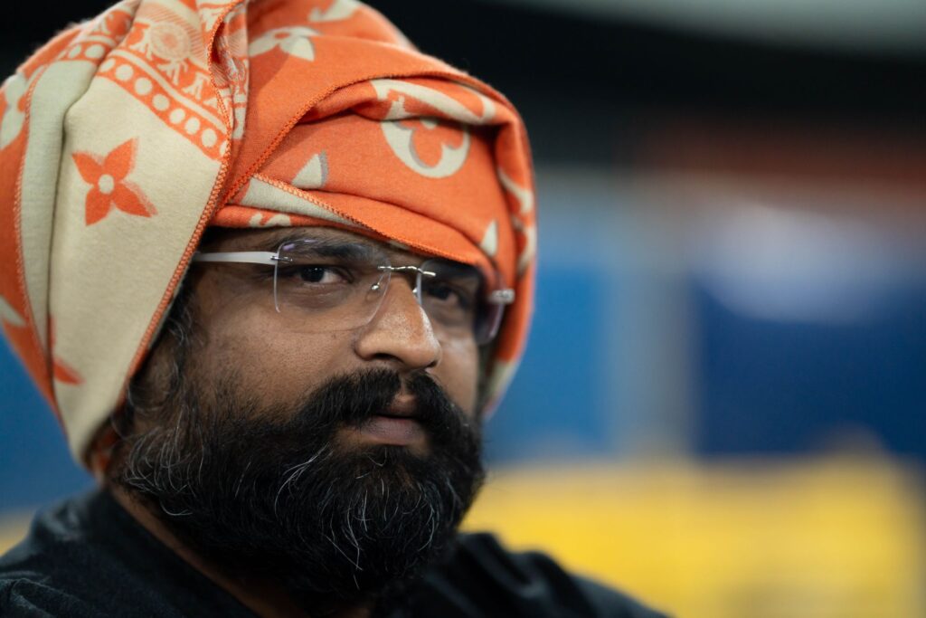 Close-up portrait of a man in a traditional orange turban with glasses, showcasing cultural heritage.