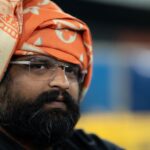 Close-up portrait of a man in a traditional orange turban with glasses, showcasing cultural heritage.