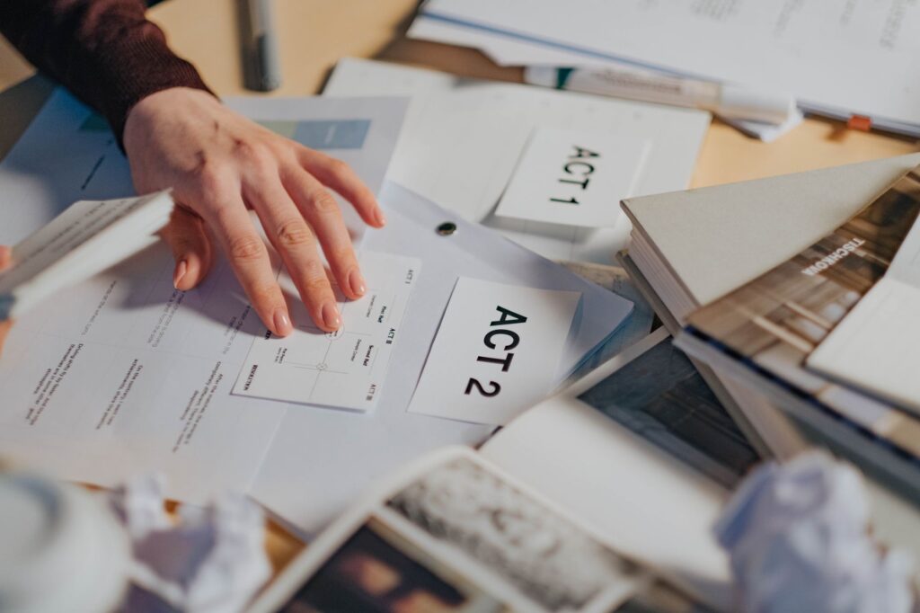 A cluttered desk with scripts, notes, and a person's hand organizing screenplay drafts.