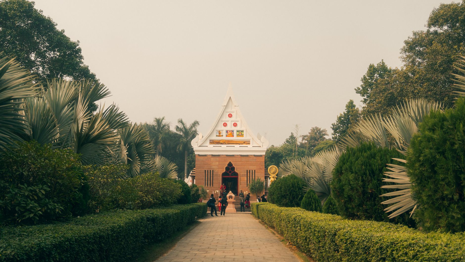 Serene temple entrance nestled in lush gardens under a clear sky, inviting visitors to explore.