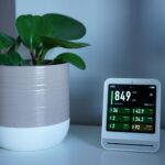 Air quality monitor next to a potted plant on a desk, showing CO2 and PM2.5 levels.