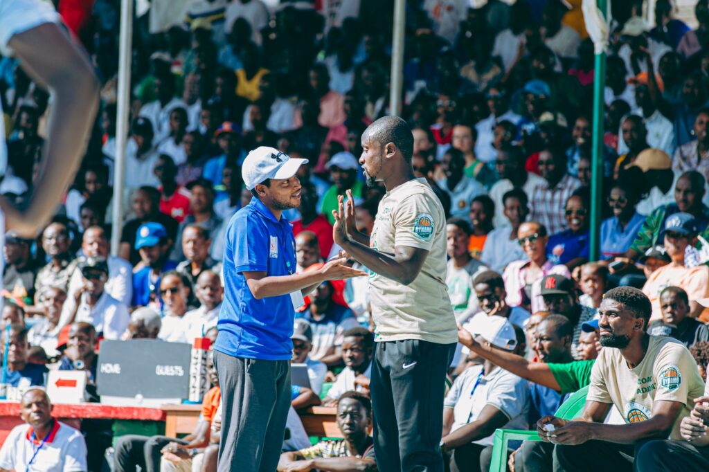 Lively outdoor basketball game scene with two coaches conversing, engaging audience in the background.